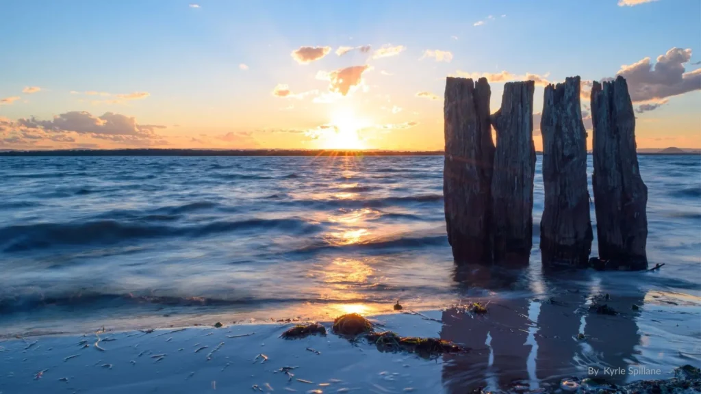 Sunset over Pumicestone Passage at Banksia Beach, Bribie Island, with wooden posts in the water and gentle waves on the shore