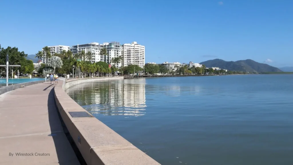 Cairns Esplanade Lagoon with waterfront walkway, tropical palm trees, and mountain backdrop in Queensland, Australia