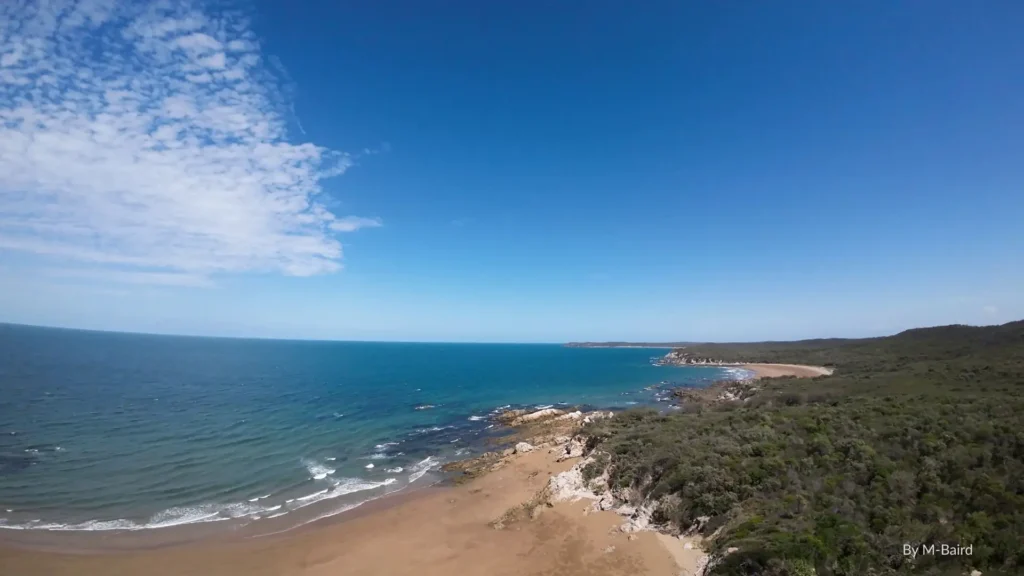 Curtis Island, Queensland, with rugged coastline, sandy beach, and forested national parklands meeting the Coral Sea