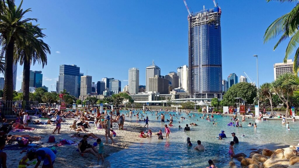 People swimming and relaxing at South Bank man-made beach in Brisbane with city skyline in the background