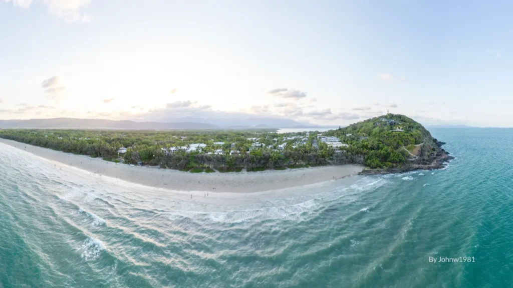 Aerial view of Four Mile Beach in Port Douglas, with palm-lined sandy shoreline, calm turquoise waters, and headland lookout, Tropical North Queensland.