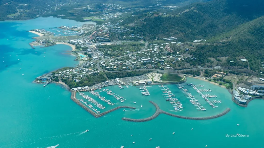 Aerial view of Airlie Beach with marinas, turquoise waters, and the town nestled against lush green hills in the Whitsundays, Queensland.
