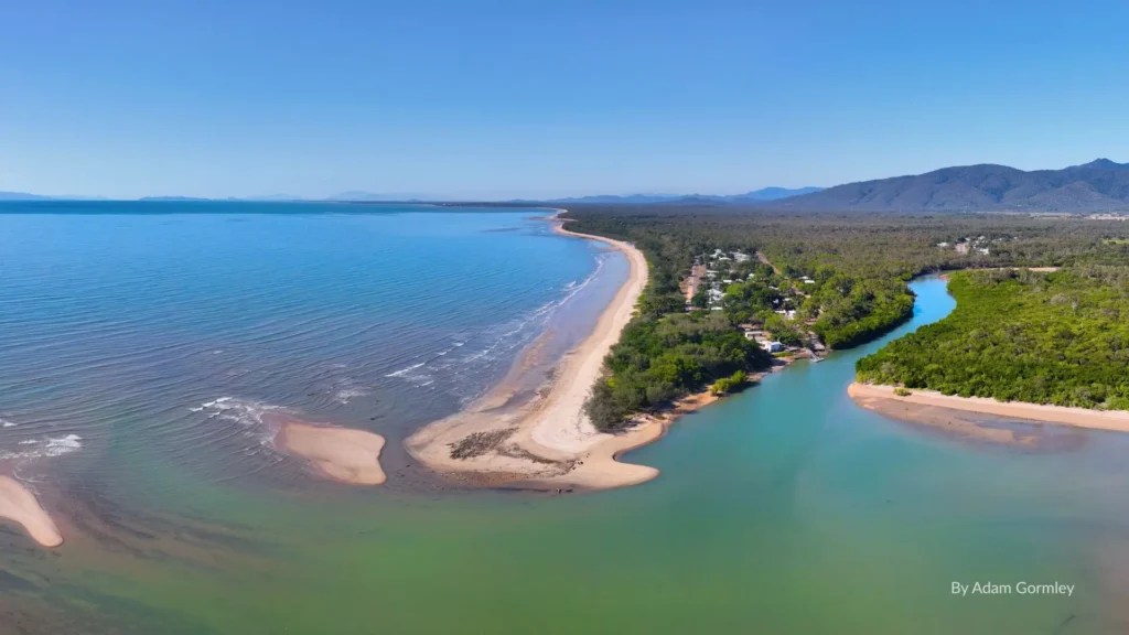 Aerial view of Balgal Beach with golden sand, calm turquoise waters, and river mouth surrounded by lush greenery, north of Townsville, Queensland.