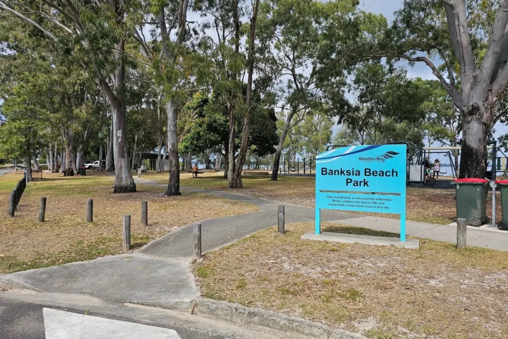 Entrance to Banksia Beach Park on Bribie Island, Queensland, featuring park sign, shaded trees, picnic areas, and foreshore access.