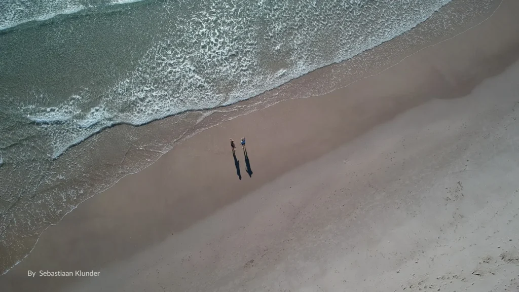 Aerial view of golden sands and gentle waves at Blacks Beach near Mackay, Queensland, with two people walking along the shoreline.