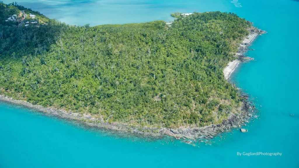 Aerial view of Cannonvale Beach with turquoise waters, green headland, and a quiet foreshore west of Airlie Beach, Whitsundays, Queensland.