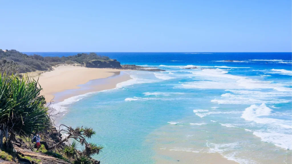 Cylinder Beach with turquoise waves rolling onto golden sand framed by rocky headlands and pandanus trees, North Stradbroke Island, Queensland.