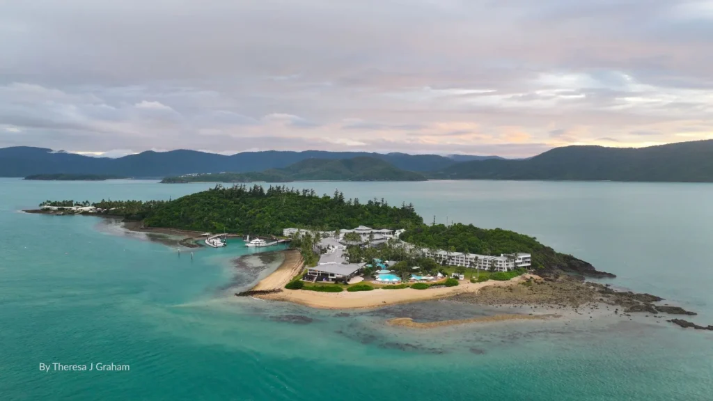 Aerial view of Daydream Island with sandy beaches, turquoise waters, and resort accommodation surrounded by lush greenery in the Whitsundays, Queensland.