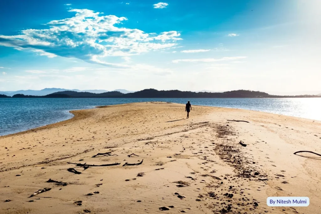 Dunk Island, Queensland – golden sandy shoreline with a lone person walking along the beach, calm waters, and mountain views near Mission Beach.
