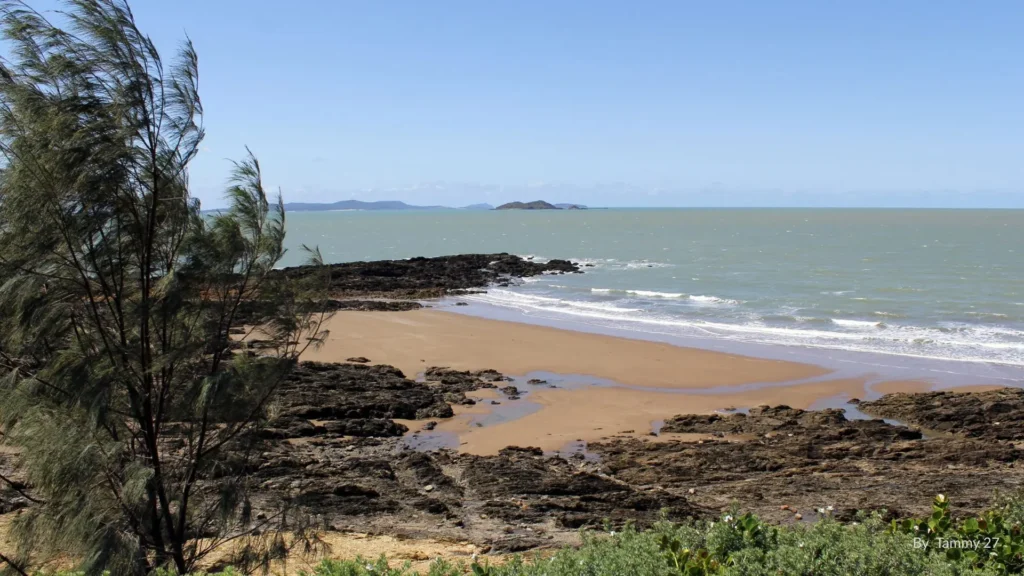 View of Emu Park Main Beach on the Capricorn Coast, Queensland, with sandy foreshore, rocky headlands, and calm coastal waters.
