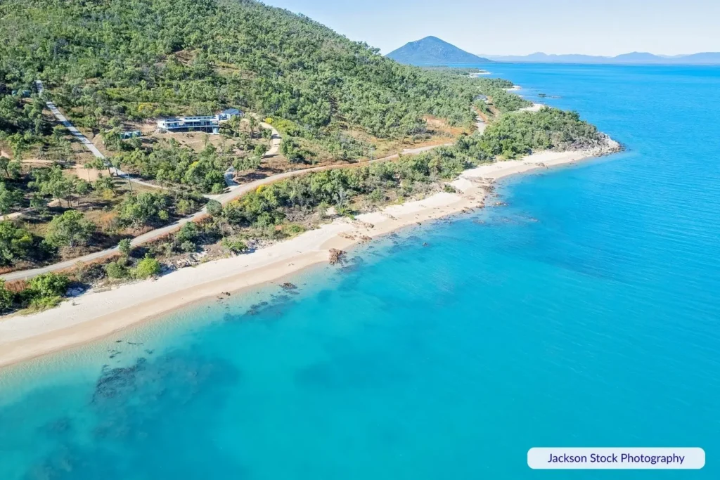 Aerial view of Gloucester Island, Whitsundays Queensland, with lush green hills, sandy beaches, and turquoise Coral Sea waters.