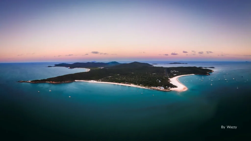 Aerial view of Great Keppel Island, Queensland, with turquoise waters, white sandy beaches, and lush green hills at sunset.