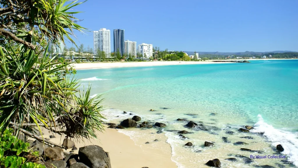 Turquoise waves at Greenmount Beach with pandanus trees and Coolangatta high-rise skyline in the distance, Gold Coast, Queensland.