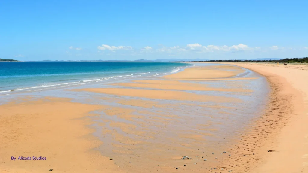 Wide sandy shoreline of Harbour Beach in Mackay, Queensland, with calm blue waters, gentle waves, and a clear summer sky.