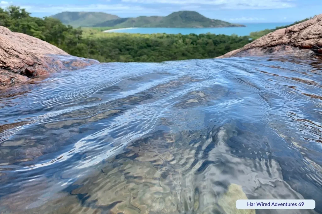 View from Hinchinbrook Island’s natural infinity pool with crystal-clear water, lush rainforest, and mountains overlooking the Coral Sea in Queensland.