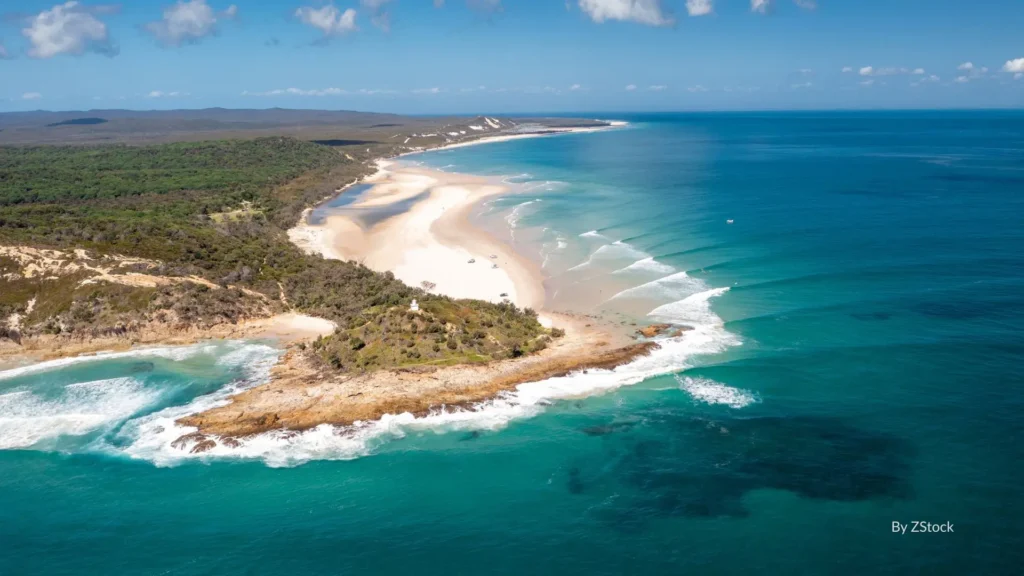 Aerial view of Honeymoon Bay, a secluded sandy cove beneath Cape Moreton’s cliffs with turquoise waters and sweeping views of the Coral Sea, Moreton Island, Queensland.