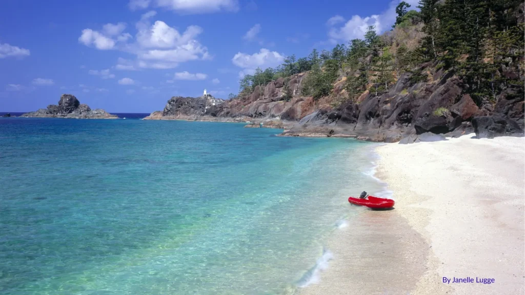 Red kayak resting on the sandy shoreline of Hook Island with turquoise waters, rocky headlands, and forested cliffs, Whitsundays, Queensland.