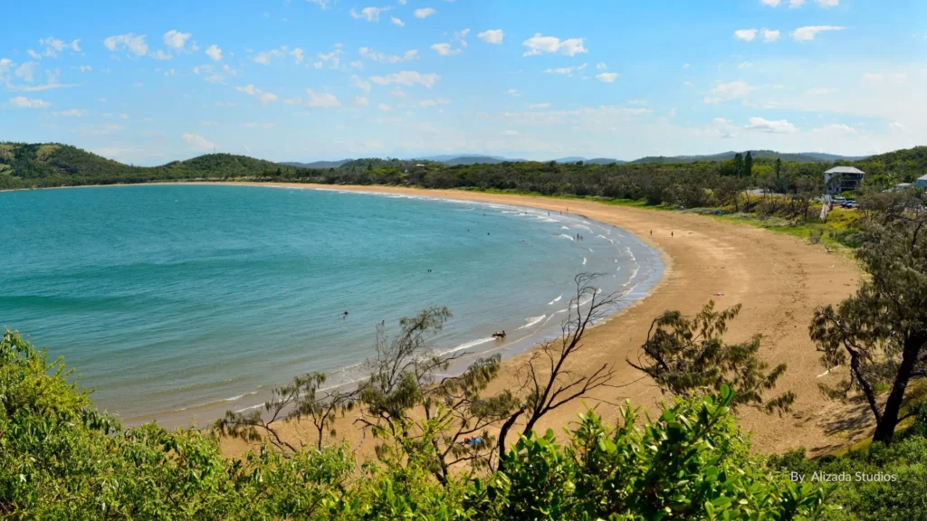 Scenic view of Kemp Beach near Yeppoon, Queensland, with calm turquoise water, golden sand, and surrounding greenery under a clear blue sky.