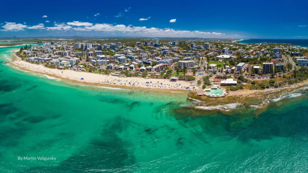 Aerial view of Kings Beach with turquoise water, sandy foreshore, tidal swimming pool, and Caloundra skyline, Sunshine Coast, Queensland.