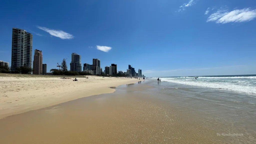 Wide sandy shoreline of Kurrawa Beach with surfers in the water and Gold Coast high-rise buildings in the background, Queensland, Australia.