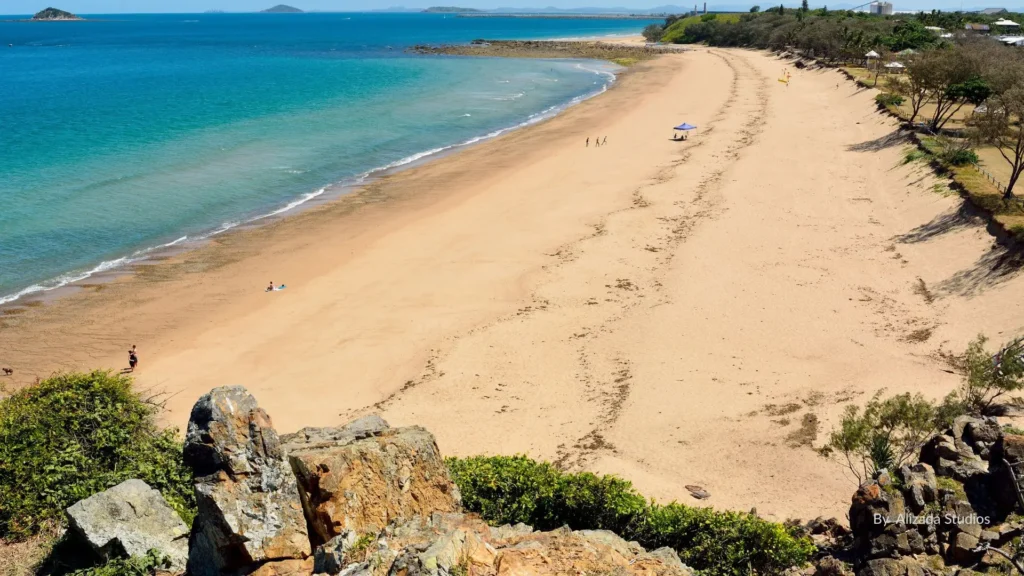 Golden sandy shoreline of Lamberts Beach with turquoise waters, rocky headland, and scattered beachgoers, Mackay, Queensland.