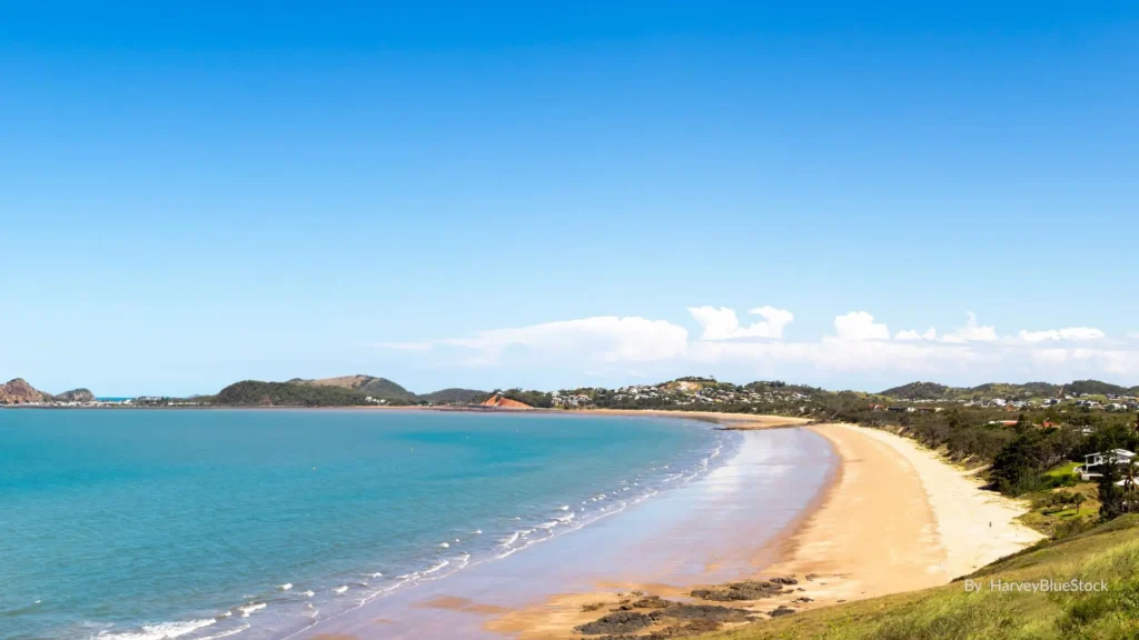 Long crescent of Lammermoor Beach with turquoise Keppel Bay, palm-lined foreshore and homes on the headland, Capricorn Coast, Queensland.