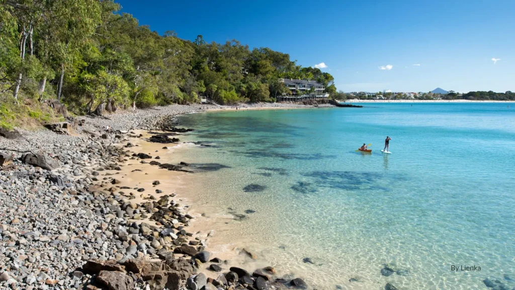 Little Cove in Noosa with clear turquoise water, rocky foreshore, and paddleboarders enjoying the calm sheltered bay, Sunshine Coast, Queensland.
