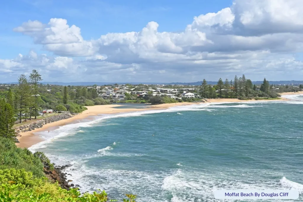 Scenic view of Moffat Beach, Sunshine Coast, Queensland, with golden sand, ocean waves, pine trees, and nearby residential area.