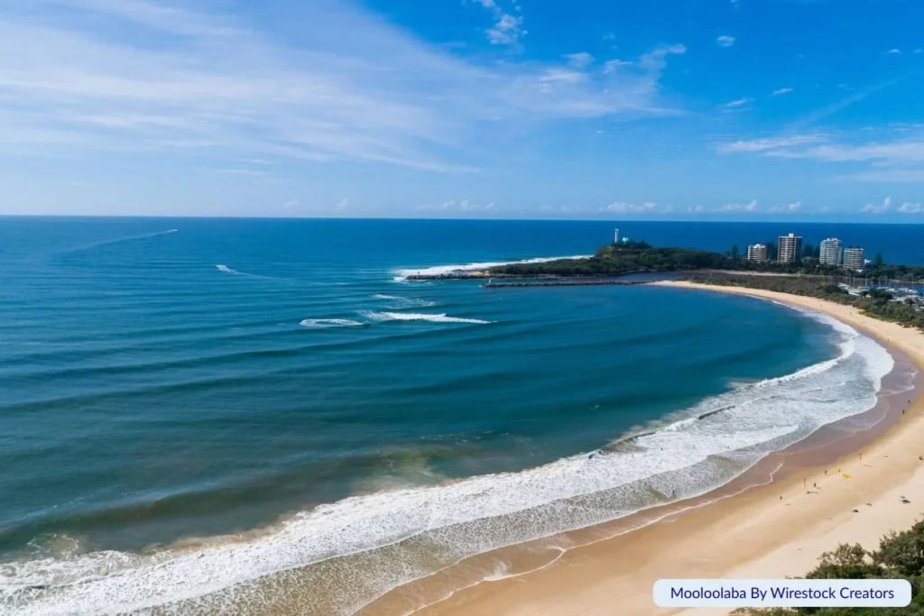 Aerial view of Mooloolaba Beach on the Sunshine Coast, Queensland, with golden sand, rolling surf, high-rise buildings, and the Mooloolaba Spit in the distance.
