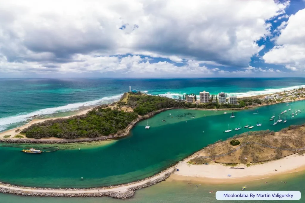 Aerial view of Mooloolaba Spit and river entrance on the Sunshine Coast, Queensland, with turquoise water, anchored boats, sandy shoreline, and high-rise buildings in the distance.