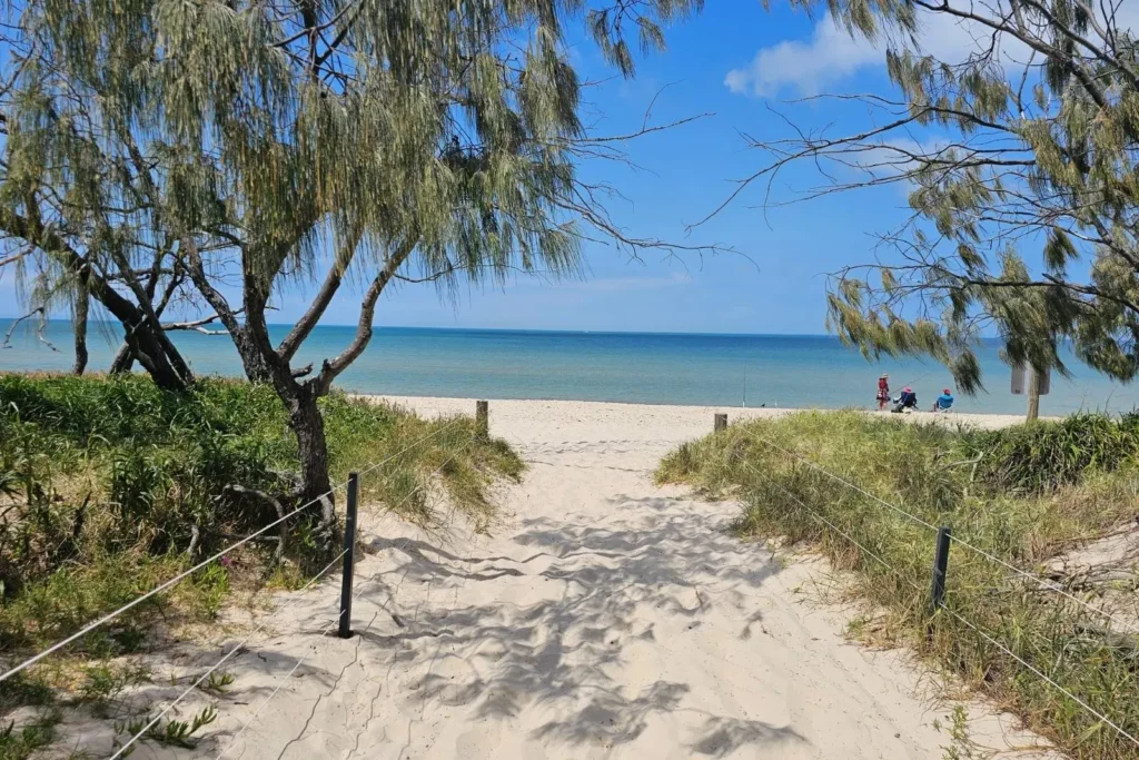 Entrance track to Red Beach on Bribie Island QLD, with sandy path through coastal trees leading to golden sand and blue ocean views