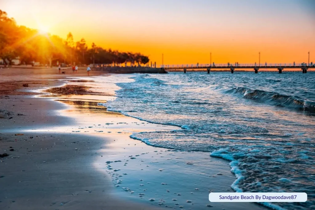 Golden sunset over Sandgate Beach in Brisbane, Queensland, with gentle waves washing onto the shoreline and the pier stretching into Moreton Bay