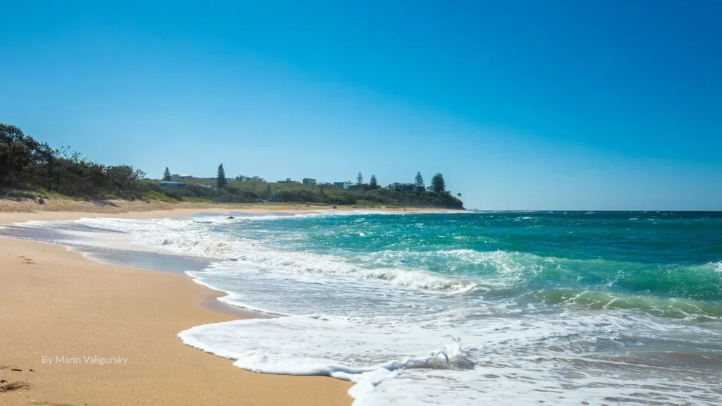 Shelly Beach with golden sand, turquoise waves, and rocky headland under a clear blue sky, Caloundra, Sunshine Coast, Queensland.