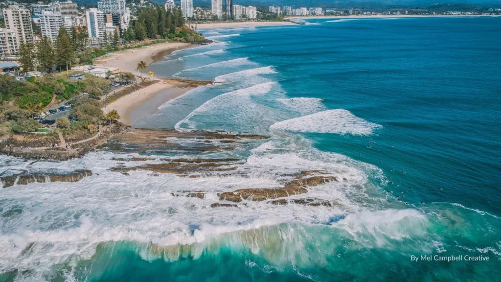 Aerial view of Snapper Rocks showing rocky headland, rolling surf, and nearby beaches with the Coolangatta skyline in the background, Gold Coast, Queensland, Australia.
