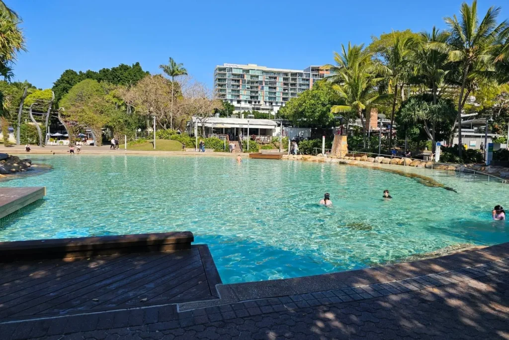 Streets Beach lagoon, South Bank Brisbane QLD, Australia — crystal-clear man-made lagoon with swimmers, palm trees, landscaped gardens and apartments.