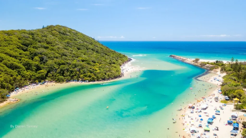 Aerial view of Tallebudgera Creek with turquoise waters, sandy shoreline, and lush green Burleigh Headland beside the creek mouth, Gold Coast, Queensland, Australia.