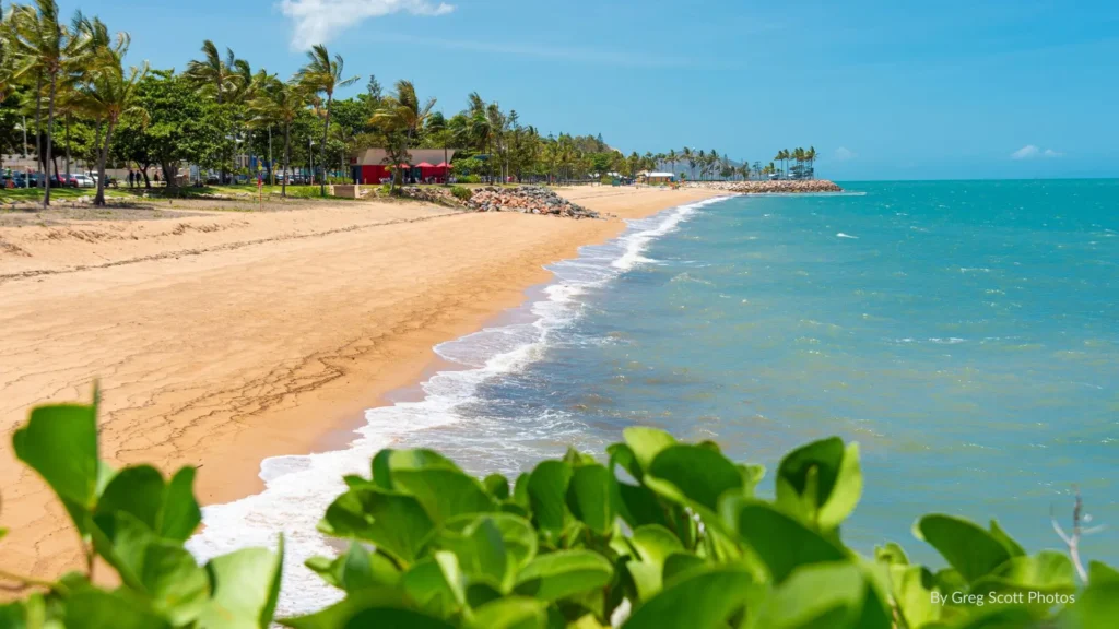 Golden sandy foreshore of The Strand in Townsville with palm trees, cafes, and turquoise waters overlooking Magnetic Island.