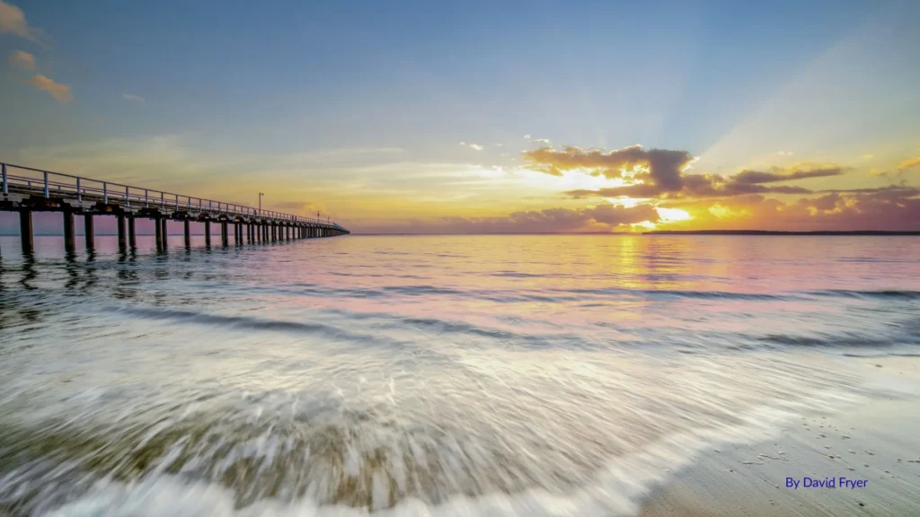Sunrise over Urangan Beach with calm waters and the historic Urangan Pier stretching into the horizon, Hervey Bay, Queensland.
