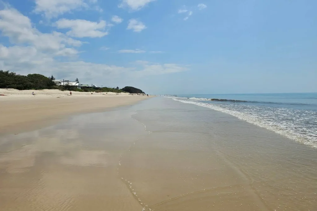 Low tide at Woorim Beach on Bribie Island QLD, with wet sandy shoreline, gentle waves, and beach houses nestled behind the dunes.