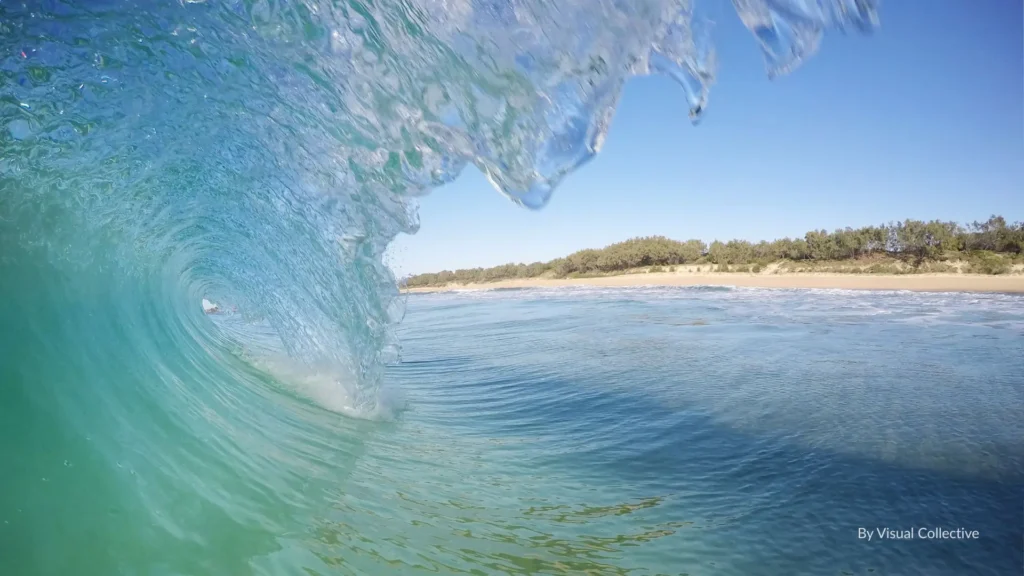 Crystal-clear wave curling towards shore with Wurtulla Beach’s sandy shoreline and coastal dunes in the background, Sunshine Coast, Queensland.