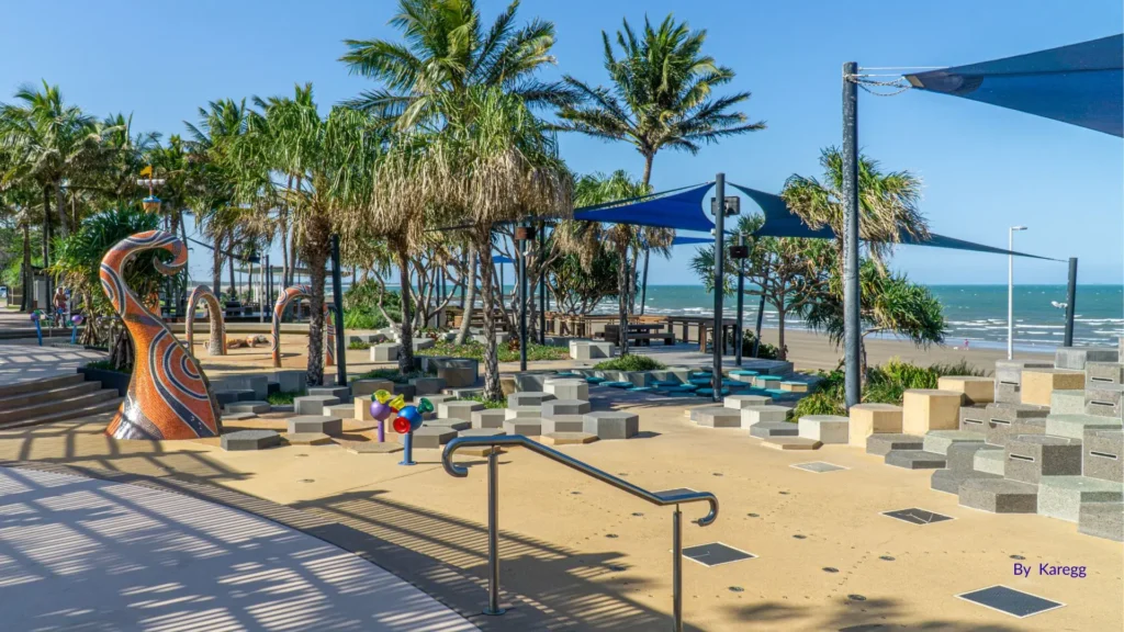 Family-friendly foreshore at Yeppoon Main Beach with palm trees, shaded seating, colourful sculptures, and sandy shoreline overlooking the Coral Sea, Capricorn Coast, Queensland.