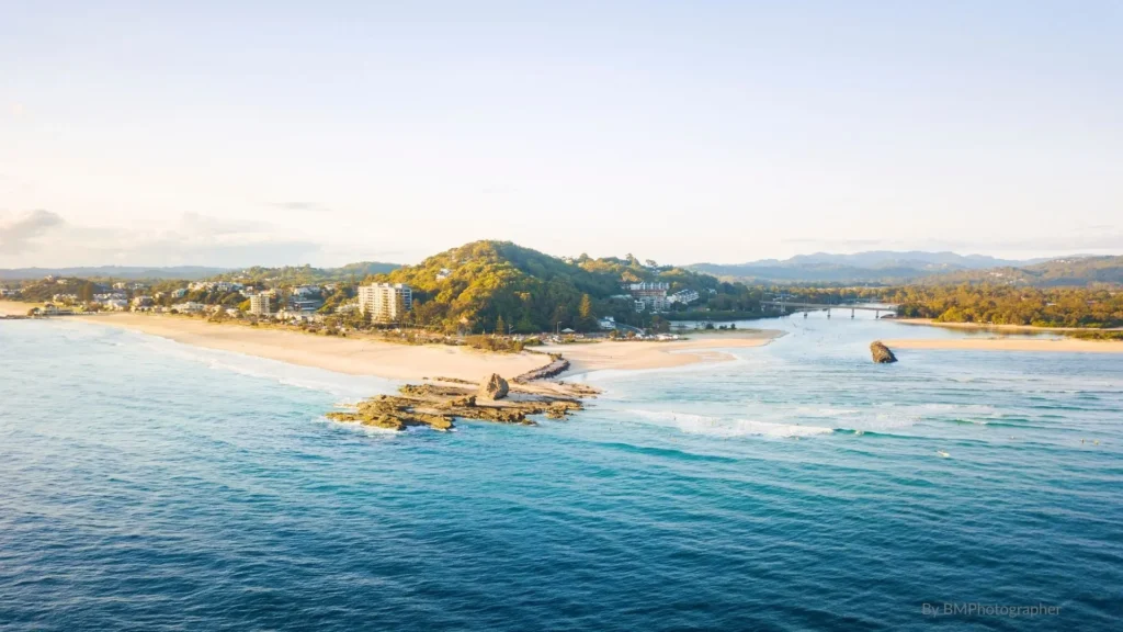 Aerial view of Currumbin Alley, Gold Coast — where Currumbin Creek meets the ocean, with sand spit, surfers, and headland