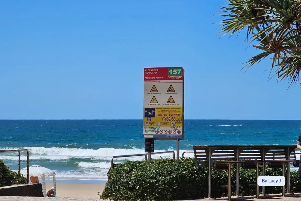Beach safety sign and lookout area overlooking clear blue surf at Alexandra Headland on the Sunshine Coast, Queensland, Australia.