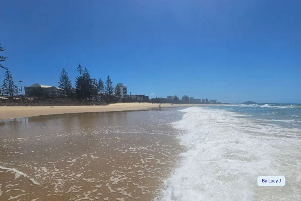 Waves rolling onto golden sand at Alexandra Headland Beach with views toward Mooloolaba, Sunshine Coast, Queensland.