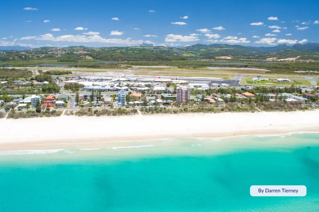 Aerial view of Bilinga Beach with turquoise water, white sand, and the Gold Coast Airport runway visible just behind the beachfront, Southern Gold Coast, Queensland.