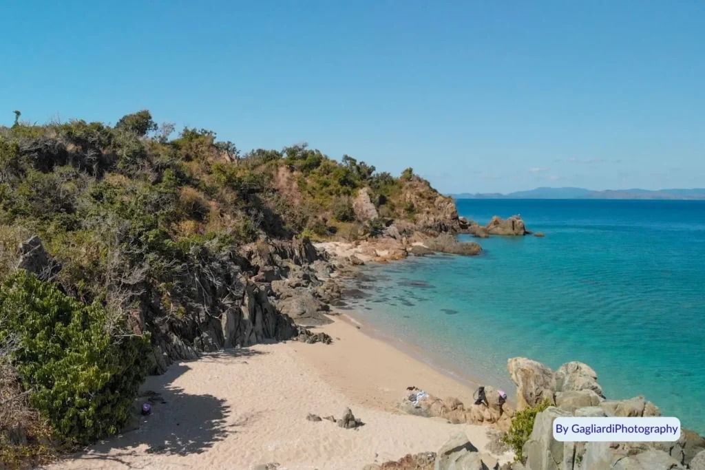 Rocky shoreline and clear blue water along the secluded beach of Black Island in the Whitsundays, Queensland.