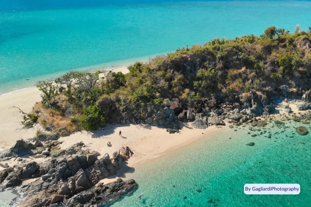 Aerial view of Black Island showing small sandy cove, rocky cliffs, and crystal-clear turquoise water, Whitsunday Islands National Park, Queensland.