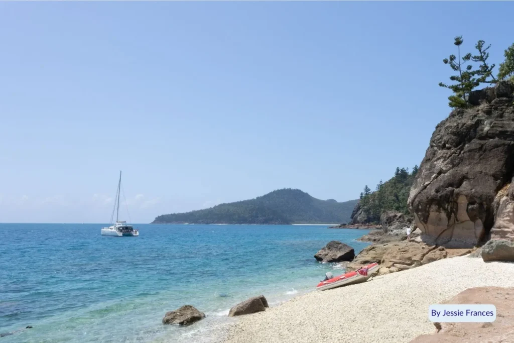 Sailboat anchored off the rocky coast of Black Island with kayaks resting on the white coral beach, Whitsunday Islands, Queensland, Australia.