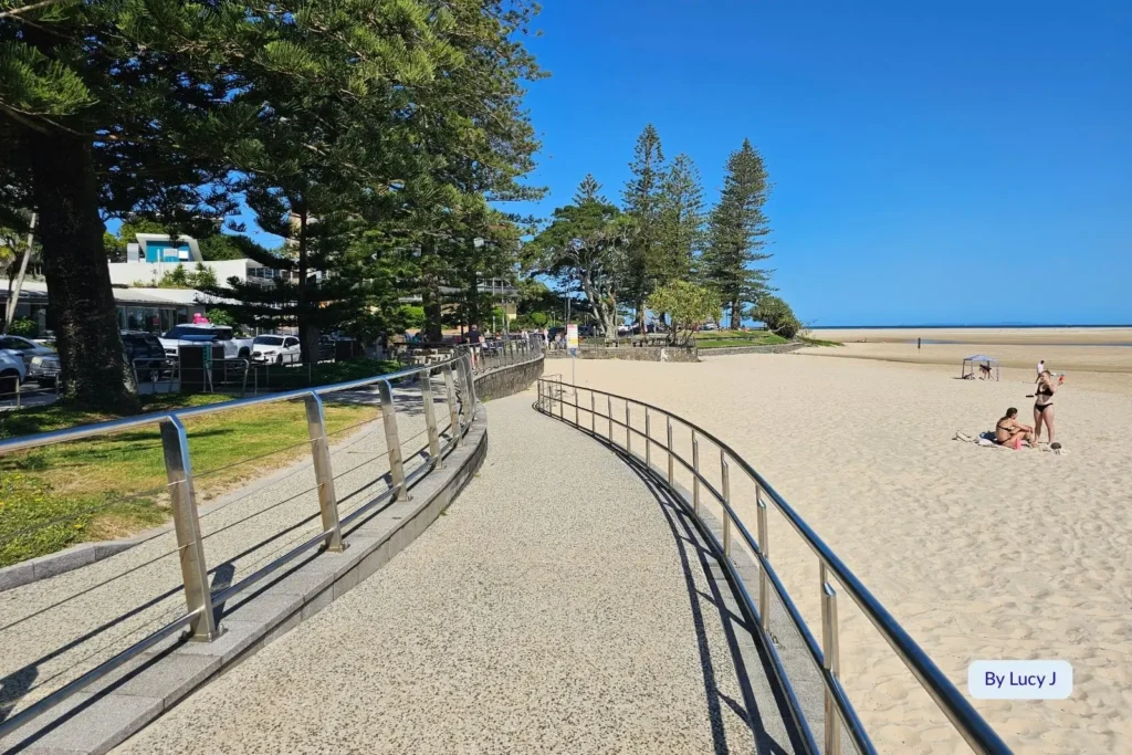 Curved foreshore path and golden sand at Bulcock Beach, Caloundra, with cafes and pine trees along the waterfront, Sunshine Coast, Queensland.