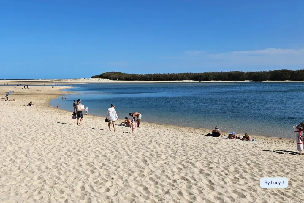 Families relaxing on the sand beside the tranquil inlet at Bulcock Beach, Caloundra, with views across Pumicestone Passage, Sunshine Coast, Queensland.